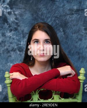 Weibliche Teenagerin sitzt auf einem lindgrünen Holzstuhl, nach hinten gedreht. Ihre Arme liegen auf der Rückseite des Stuhls. Stockfoto