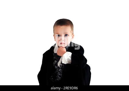 Der kleine Junge kniet nieder und legt sein Kinn auf die Hand. Er trägt einen schwarz-silbernen Smoking. Sein Gesichtsausdruck ist feierlich. Stockfoto