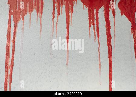 Rote Düsen an der Wand. Farbe fließt nach unten. Blut auf der Oberfläche. Vandalismus bei Baudetails. Textur der aktuellen Tinte. Stockfoto