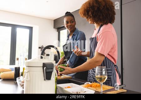 Glückliches, vielfältiges Paar, das das Essen zubereitet, Gemüse wäscht und sich in der Küche unterhält Stockfoto