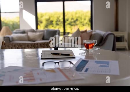 Nahaufnahme von Notizbuch, Tasse Tee, Dokumenten und Gläsern auf dem Tisch im Wohnzimmer Stockfoto
