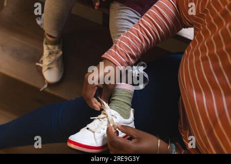 Mittelteil afroamerikanischer Mutter und Tochter, die vor der Schule zu Hause Schnürsenkel binden Stockfoto