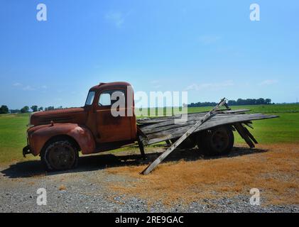 Ein alter Flachbettlaster rostet unter der Sommersonne im Nordwesten von Arkansas. Reifen sind trocken verrottet und platt. Die Felder erstrecken sich hinter dem Lkw. Stockfoto