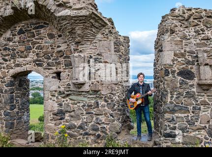 Der einsame Musiker Mike Baillie spielt Gitarre in den Ruinen der St. Anthony's Chapel, Holyrood Park, Edinburgh, Cotland, Großbritannien Stockfoto