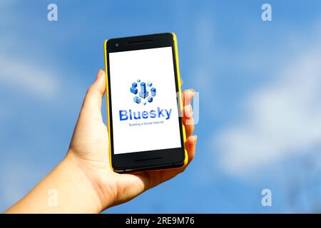 BlueSky-App. Handheld-Smartphone in gelber Kunststoffhülle auf blauem Himmel Naturhintergrund. Blue Sky ist eine neue Social-Media-App und Textfreigabe Stockfoto