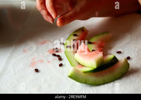 Eine Frau genießt eine köstliche Wassermelone, die zu Hause ein Stück in der Hand hält. Die Nahaufnahme erfasst die lebendigen Farben und die saftige Textur der Früchte Stockfoto