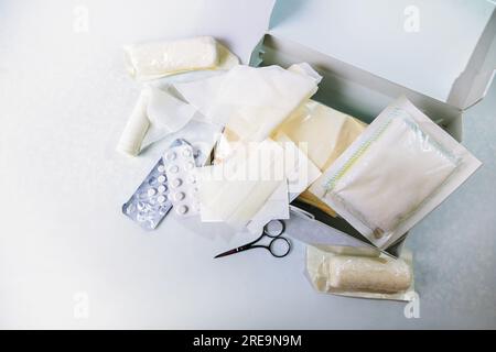 Öffnen Sie den erste-Hilfe-Kasten für Reisen und als Hausarzttruhe mit Verbänden, Pflastern, Pillen und Scheren, Gesundheits- und medizinisches Konzept, hellgraue Hintergrunen Stockfoto