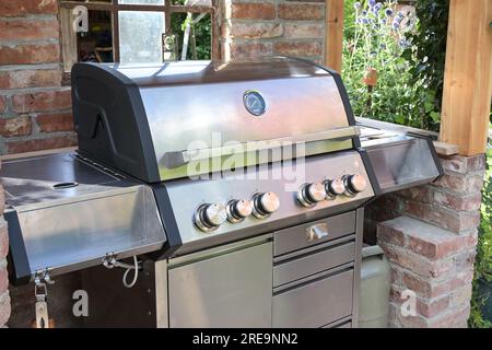 Moderner Grill aus Edelstahl in einem Unterstand aus alten Ziegeln im Garten, Kochkonzept im Freien, ausgewählter Fokus, schmaler Bereich Stockfoto