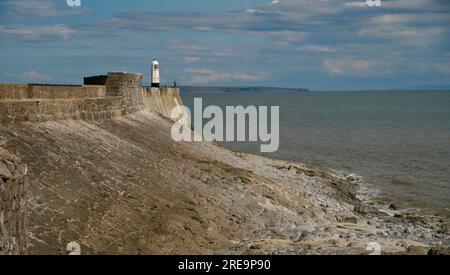 Porthcawl, Wales, Küstenlandschaft bei Ebbe mit einem launischen, bewölkten Himmel; der Leuchtturm befindet sich in der Ferne und ist ein beliebter Ort für Fischer Stockfoto