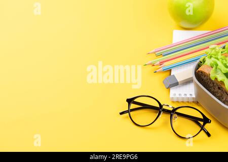 Schulbedarf, Schreibwaren und Lunchbox auf gelbem Hintergrund. Bildung und Ernährung. Mit Leerzeichen Stockfoto