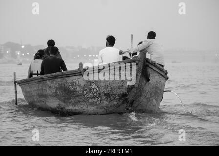 Leute in einem Boot auf dem ganges bei Veranassi. Die Menschen bereiten in Varanasi am Ufer des Ganges, einer der ältesten bewohnten Städte der Welt und die heiligste der sieben heiligen Städte des Hinduismus, Scheiterhaufen vor. Jeden Tag werden in Manikarnika Ghat, dem größten und vielversprechendsten Einäscherungsghat, rund 100 Leichen auf Holzscheiterhaufen am Flussufer eingeäschert. Die ewige Flamme, die die Feuer nährt, soll seit Jahrhunderten brennen. Varanasi, Indien. Stockfoto