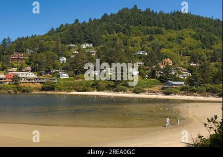 In einer malerischen Kleinstadt an der Küste von Oregon, USA, könnt ihr am Strand entlang spazieren gehen und unter den Häusern an den Hügeln spazieren Stockfoto