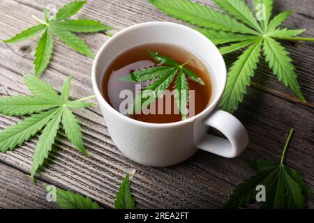Tee mit Cannabisblättern auf einem Holztisch. Medizinischer Kräutertee mit Marihuana aus der Nähe Stockfoto