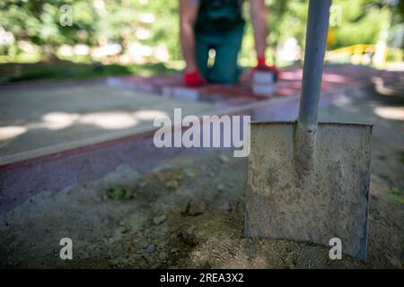 Im Vordergrund, eine Schaufel im Boden und Bauarbeiter im Hintergrund. Stockfoto