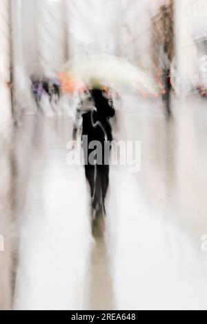 Ein Mann im Regen, der mit einem Regenschirm in der Stadt spaziert. Nicht erkennbare Person in Bewegung verschwimmt Stockfoto