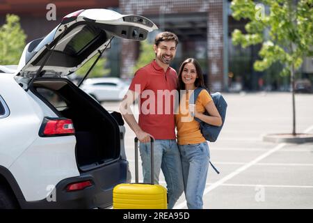 Glückliches junges Paar Touristen, die sich neben dem Auto am Flughafen posierten Stockfoto