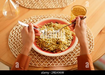 Lady isst leckere italienische Pasta mit Parmesankäse, hält Gabel und Löffel, Spaghetti wickeln sie um eine Gabel, pov-Shot Stockfoto