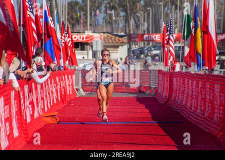 Huntington Beach, Kalifornien, USA. 21. April 2018. Die erste Läuferin in einem Triathlon-Wettkampf in Huntington Beach, Kalifornien, geht auf einer roten Strecke die Ziellinie entlang, während Flaggen schwärmen und Zuschauer jubeln. (Kreditbild: © Spencer Grant/ZUMA Press Wire) NUR REDAKTIONELLE VERWENDUNG! Nicht für den kommerziellen GEBRAUCH! Stockfoto