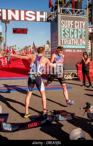 Huntington Beach, Kalifornien, USA. 21. April 2018. Der Sieger eines Triathlon-Wettkampfs in Huntington Beach, Kalifornien, gratuliert dem Gewinner des zweiten Platzes, der die Ziellinie überquert. Achten Sie auf das Band des Gewinners im Vordergrund. (Kreditbild: © Spencer Grant/ZUMA Press Wire) NUR REDAKTIONELLE VERWENDUNG! Nicht für den kommerziellen GEBRAUCH! Stockfoto