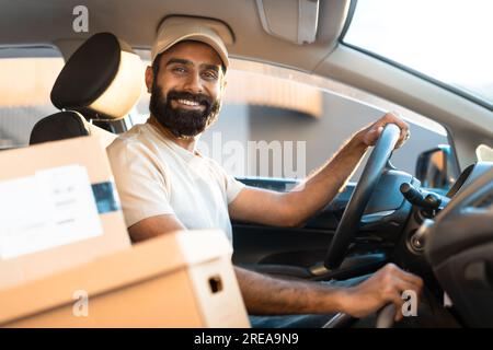 Fröhlicher Arabischer Fahrer Sitzt Im Auto Zwischen Kartons Stockfoto