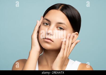 Nahaufnahme eines glücklichen Mädchengesichts mit natürlichem gekämmtem Haar, das gut gepflegte, reine, perfekte Haut berührt Stockfoto