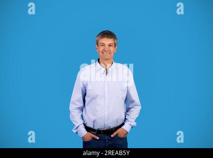 Fröhlicher, reifer Mann mit grauen Haaren, der auf blauem Hintergrund steht Stockfoto