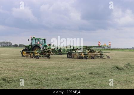 Niedrige Sicht auf einen Traktor mit großem Heurechen auf einem Grasfeld in der niederländischen Landschaft Stockfoto