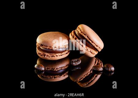 Aromatisierte farbige Makronen auf reflektierender Oberfläche mit Kaffeebohnen Stockfoto