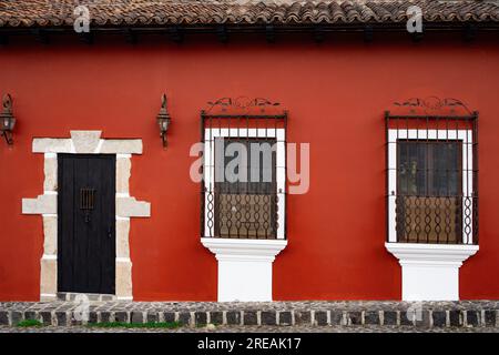 Vordertür und Fenster mit Sicherheitsbügeln in einem rot gestrichenen kleinen, alten Haus in Guatemala Stockfoto