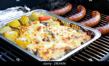 Gegrilltes Gemüse und Fleischwürste auf rostfreiem Grill mit Flammen auf dunklem Hintergrund. Speise- und Küchenkonzept Stockfoto