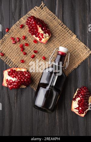 Reifer Granatapfel, verstreute große Körner, frisch gepresster Granatapfelsaft in einer transparenten Flasche auf einem hölzernen Hintergrund von oben. Kreativ Stockfoto