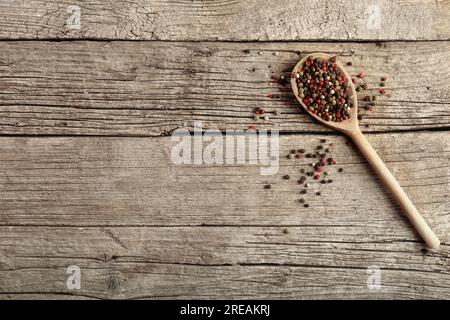 Mischung aus Paprika und Erbsen in einem Holzlöffel auf Holzhintergrund, Draufsicht. Roter Pfeffer, weißer Pfeffer und grüner Pfeffer. Stockfoto