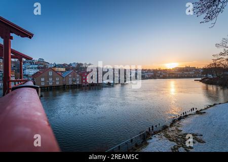 Malerischer Blick auf Trondheim und den Nidelva River von der Old Town Bridge oder Gamle Bybro bei Sonnenuntergang im Winter vor blauem Himmel Stockfoto