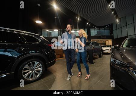 Glückliches Ehepaar, das den Kauf eines Autos in einem Ausstellungsraum feiert. Stockfoto