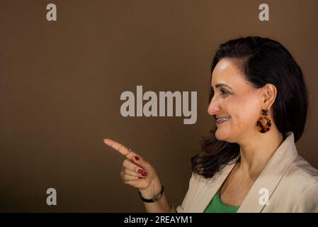 Porträt lächelnd und selbstbewusste Coaching-Frau, die Gesten von Hand macht. Motivierendes und demokratisches Management. Isoliert auf braunem Hintergrund. Stockfoto