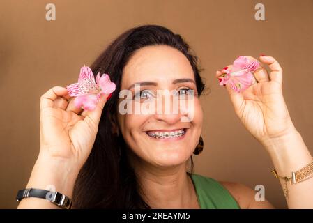 Eine Frau, weiß, sehr glücklich und verliebt, die eine Orchideenblume neben ihren Augen hält. Isoliert auf braunem Hintergrund. Stockfoto