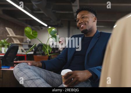Ein glücklicher afroamerikanischer Mann, der eine Kaffeetasse im Büro hält Stockfoto