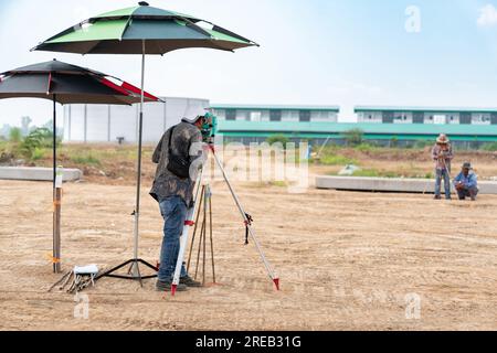 Ein Vermessungsarbeiter mit Theodolite-Ausrüstung führt Messungen am Tachymeter durch und gibt Daten auf der Baustelle ein Stockfoto