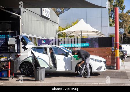 Handwaschservice in Sydney, Australien, Mitarbeiter bei Autowaschanlage reinigt ein weißes Auto mit offenen Türen, Australien, 2023 Stockfoto