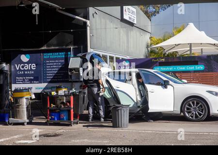 Handwaschservice in Sydney, Australien, Mitarbeiter bei Autowaschanlage reinigt ein weißes Auto mit offenen Türen, Australien, 2023 Stockfoto