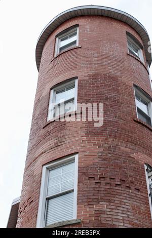 Flacher Blick auf einen geschwungenen roten Backsteinturm in einem historischen Wohn- oder Geschäftsgebäude mit Reihen von weiß gerahmten Fenstern vor einer Überkerung Stockfoto