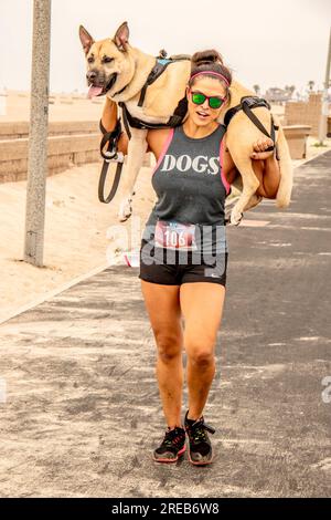 Huntington Beach, Kalifornien, USA. 14. April 2019. Eine begeisterte Hundebesitzerin trägt ihr dreibeiniges Haustier über die Ziellinie eines 10K km langen „Doggie Dash“-Rennens auf einem Pfad am Meer in Huntington Beach, CA. "Er braucht Hilfe," erklärte sie. (Kreditbild: © Spencer Grant/ZUMA Press Wire) NUR REDAKTIONELLE VERWENDUNG! Nicht für den kommerziellen GEBRAUCH! Stockfoto