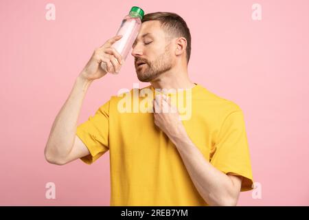 Ein müder Mann leidet an Hitze und Blutdruck, legt eine Flasche kaltes Wasser auf die Stirn, fühlt sich durstig Stockfoto