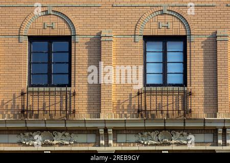 Vollformattexturhintergrund mit einer wunderschönen beigefarbenen Ziegelfassade im amerikanischen Stil des frühen 20. Jahrhunderts und dekorativen bogenförmigen Fensterrahmen Stockfoto