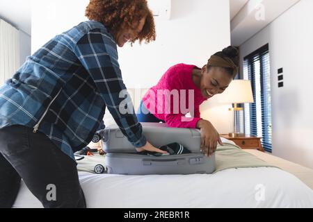 Glückliches, vielseitiges Paar, das den Koffer im Schlafzimmer zuhause zusammenschließt Stockfoto