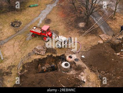 Reparatur von Abwasserrohren in einem Abwasserschacht. Wasser aus einer Kanalisation Pumpen. Der Traktor zog einen großen industriellen Kompressor an. plu Stockfoto