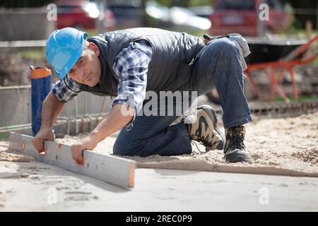 Der Meister in gelben Handschuhen legt Pflastersteine in Schichten Stockfoto