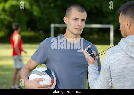 Der Fußballtrainer spricht mit einem Teenager, während er eine Stoppuhr hält Stockfoto