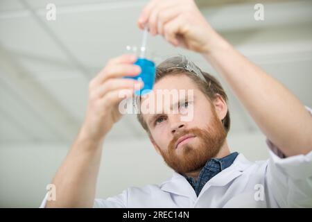 Männlicher Wissenschaftler, der Flüssigkeit in einem Kolben rührt Stockfoto