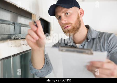 Bauinspektor, der neben einer Leiter steht und ein Klemmbrett hält Stockfoto